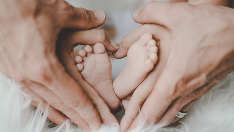 les mains de papa et maman en forme de coeur autour des pieds de bébé - 1000 premiers jours bébé