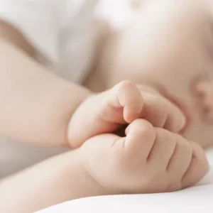 Gros plan d'un bébé qui dort paisiblement sur le côté, les mains jointes près de son visage, illustrant un sommeil serein et sécurisé.