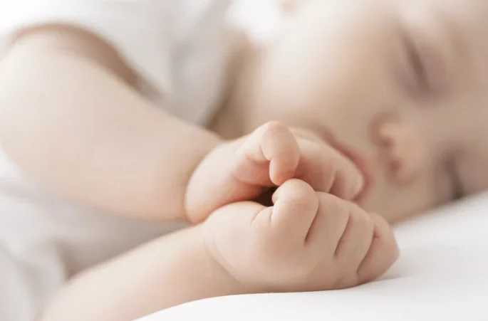 Gros plan d'un bébé qui dort paisiblement sur le côté, les mains jointes près de son visage, illustrant un sommeil serein et sécurisé.