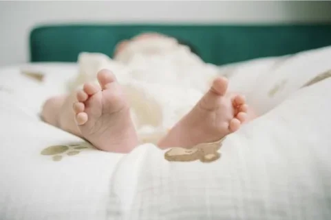 Gros plan sur les petits pieds nus d'un bébé allongé sur un linge blanc, illustrant la vérification de la température corporelle et le bien-être.