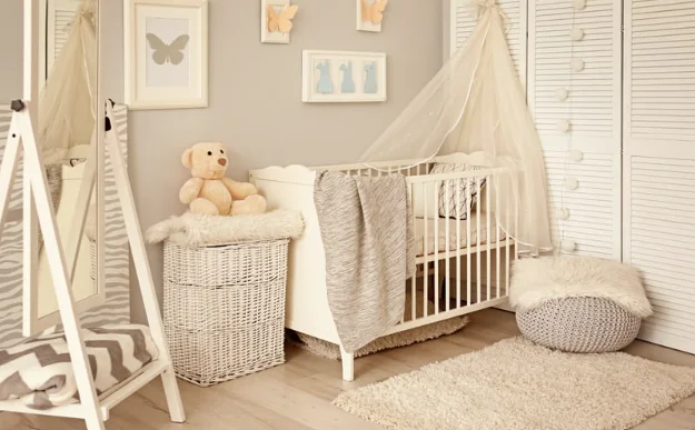 Une chambre de bébé décorée dans un style bohème et naturel. Un lit blanc avec baldaquin, un grand miroir en A, un coffre en osier blanc, des cadres d'animaux au mur et une plante en pot.