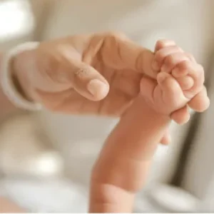 Main d'un adulte tenant doucement la petite main d'un nouveau-né à la peau sensible.