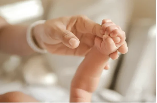 Main d'un adulte tenant doucement la petite main d'un nouveau-né à la peau sensible.